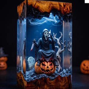 Könnte beinhalten: Eine rechteckige Kunstharzlampe mit einer Ghostface-Figur, die auf einem geschnitzten Kürbis sitzt. Die Figur hält ein Messer und ein Telefon. Ein Grabstein mit der Aufschrift R.I.P. und ein kahler Baum sind enthalten. Basis und Deckel aus Holz.