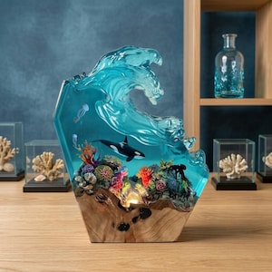 Può includere: Una scultura decorativa in resina con un'onda oceanica blu traslucida che si infrange su una base in legno. La scena include un'orca bianca e nera, barriere coralline colorate e piccole figure di meduse incorporate nel materiale blu.