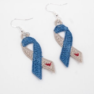 May include: A pair of silver dangle earrings with blue and beige ribbon charms. The ribbons are embroidered with a red heart.