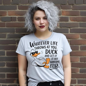 Puede incluir: Camiseta gris claro con un gráfico humorístico de un pato con gafas de sol y el texto: "WHATEVER LIFE THROWS AT YOU, DUCK AND LET IT HIT SOMEONE ELSE." La camiseta es de cuello redondo.