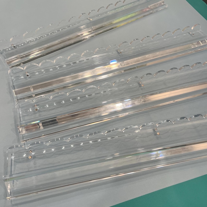 May include: Clear acrylic display shelves with scalloped edges. The shelves are rectangular and have a clear, transparent appearance. The design includes a metal support structure. The shelves are designed for displaying items.
