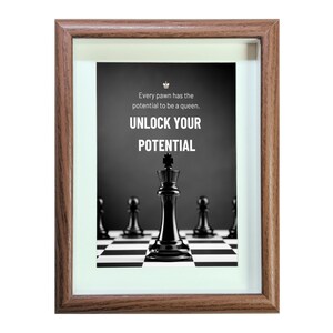 May include: A framed motivational poster with a black and white image of a chessboard with a black king in the center. The text on the poster reads "Every pawn has the potential to be a queen. UNLOCK YOUR POTENTIAL."