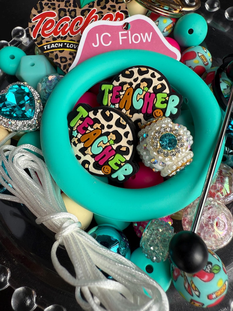 Puede incluir: Un anillo de silicona turquesa con dos dijes de "Teacher" de estampado de leopardo, un dije de pedrer&iacute;a turquesa y una variedad de cuentas de colores, incluyendo turquesa, rosa, blanco y negro.