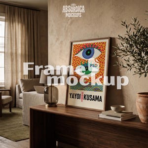 May include: A rectangular framed art print featuring a vibrant graphic illustration of two stylized eyes with blue and green irises set against a yellow and red geometric background, with the text YAYOI KUSAMA printed in bold black letters at the bottom.