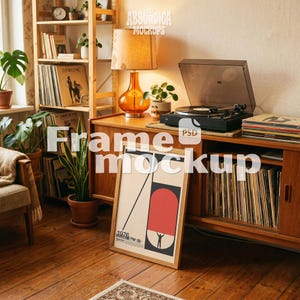 May include: A rectangular wooden picture frame leaning against a wooden cabinet. The frame contains a graphic poster with a cream background, a large red semi-circle, a black diagonal line, and a small silhouette figure holding up the red shape.
