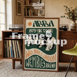 May include: A vertical rectangular poster in a wooden frame featuring the text ABBA 1979 UK TOUR WED. NOV. 5. LONDON WEMBLEY ARENA. The design includes a stylized orange sun and black and white portraits of four individuals on a dark green background.