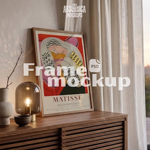 May include: A framed Matisse exhibition poster from Aix-en-Provence, dated 8 Juillet - 31 Aout 1960, featuring a stylized illustration of a person in a head covering. The poster is displayed in a wooden frame on a slatted wooden surface.
