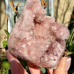 Op de afbeelding: Een grote, ruwe, roze amethistgeode met een kristallijne structuur. De geode heeft een ruwe, getextureerde buitenkant en een holte gevuld met kleinere kristallen. De kleur varieert van lichtroze tot een diepere roodachtig-roze tint.