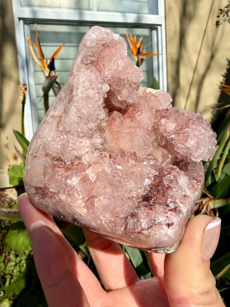 Op de afbeelding: Een grote, ruwe, roze amethistgeode met een kristallijne structuur. De geode heeft een ruwe, getextureerde buitenkant en een holte gevuld met kleinere kristallen. De kleur varieert van lichtroze tot een diepere roodachtig-roze tint.