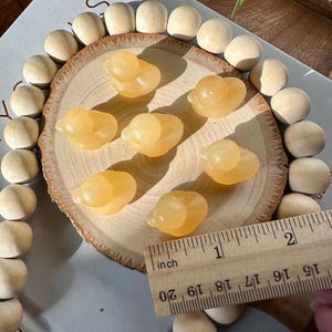 Op de afbeelding: Zes kleine, doorschijnende gele eendenbeeldjes zijn gerangschikt op een houten schijf. Een houten liniaal toont dat de eenden ongeveer 2,5 cm lang zijn. De eenden zijn omgeven door houten kralen.