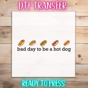 May include: White DTF transfer with five hot dogs and the text "bad day to be a hot dog". The top of the transfer reads "DTF TRANSFER" and the bottom reads "READY TO PRESS".