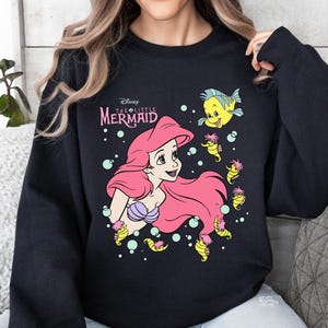 Retro vintage Ariel The Little Mermaid shirt featuring a nostalgic design with Ariel and Flounder. Made from soft, comfortable fabric for all-day wear. Perfect for Disney fans, princess lovers, and classic animation enthusiasts. Great for theme park visits, casual outfits, or as a unique gift. Available in multiple sizes and colors to match any style. A stylish and fun way to showcase love for this beloved Disney character.