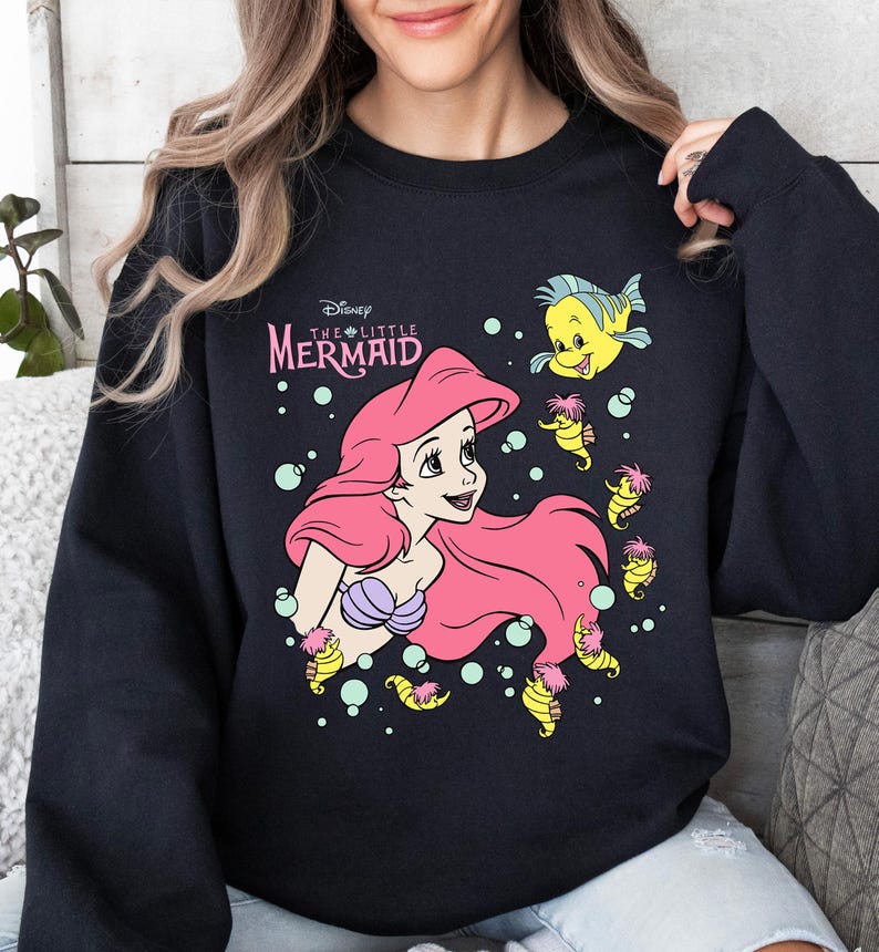 Retro vintage Ariel The Little Mermaid shirt featuring a nostalgic design with Ariel and Flounder. Made from soft, comfortable fabric for all-day wear. Perfect for Disney fans, princess lovers, and classic animation enthusiasts. Great for theme park visits, casual outfits, or as a unique gift. Available in multiple sizes and colors to match any style. A stylish and fun way to showcase love for this beloved Disney character.