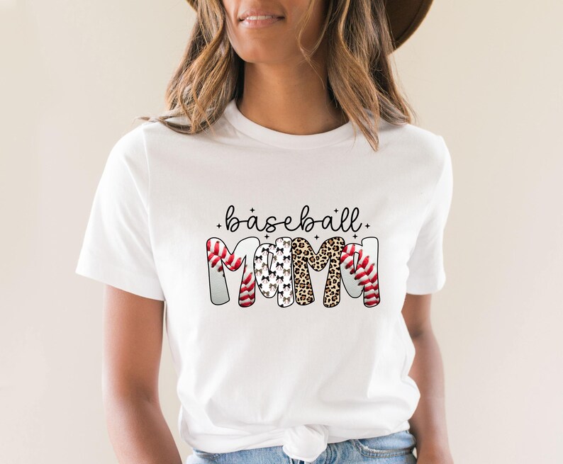 Peut inclure: T-shirt blanc avec l'inscription "baseball mom" en &eacute;criture noire. Le mot "MOM" est con&ccedil;u avec des balles de baseball, des silhouettes de chiens et des motifs l&eacute;opard. Un t-shirt d&eacute;contract&eacute; pour tous les jours.