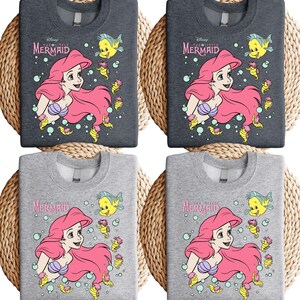 Retro vintage Ariel The Little Mermaid shirt featuring a nostalgic design with Ariel and Flounder. Made from soft, comfortable fabric for all-day wear. Perfect for Disney fans, princess lovers, and classic animation enthusiasts. Great for theme park visits, casual outfits, or as a unique gift. Available in multiple sizes and colors to match any style. A stylish and fun way to showcase love for this beloved Disney character.