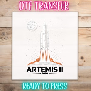 May include: White DTF transfer featuring a rocket launching into space, with the text "ARTEMIS II 2026". The design includes a moon and stars, with the words "READY TO PRESS" at the bottom. The words "DTF TRANSFER" are at the top.