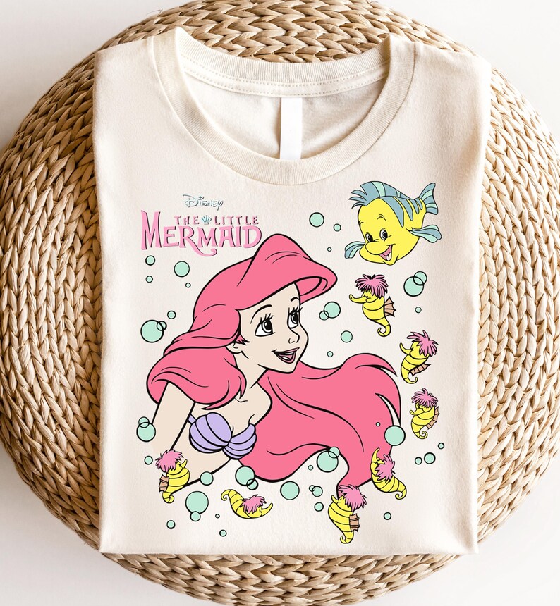 Retro vintage Ariel The Little Mermaid shirt featuring a nostalgic design with Ariel and Flounder. Made from soft, comfortable fabric for all-day wear. Perfect for Disney fans, princess lovers, and classic animation enthusiasts. Great for theme park visits, casual outfits, or as a unique gift. Available in multiple sizes and colors to match any style. A stylish and fun way to showcase love for this beloved Disney character.