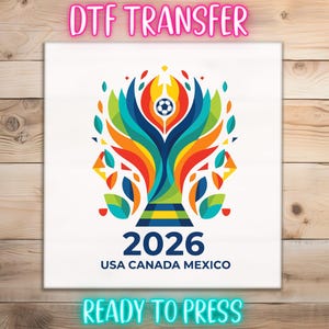 May include: A white DTF transfer with a colorful graphic of a soccer ball inside a stylized design. The text "2026 USA CANADA MEXICO" is below the graphic. The words "DTF TRANSFER" and "READY TO PRESS" are also displayed.