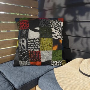 Può includere: Un cuscino quadrato con un design patchwork composto da vari motivi animalier in diversi colori, tra cui rosso, nero, bianco, giallo e verde. Il tessuto presenta una griglia di texture e motivi grafici distinti su tutta la superficie.