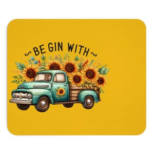 May include: A yellow mousepad features a teal vintage truck filled with sunflowers. The truck has a wooden bed and is decorated with a sunflower on the door. The text "BEGIN WITH" is arched above the truck.