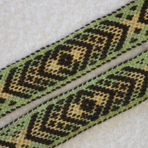 May include: Two woven bands with a geometric pattern. The bands feature a repeating design of black diamonds and yellow crosses on a green background. The bands are likely used for decorative purposes.