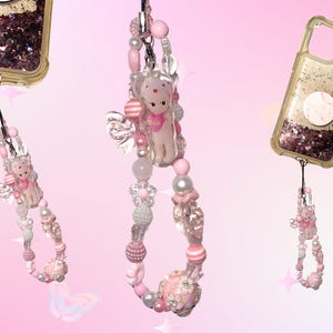 May include: Pink and white beaded phone charms with a small bear figurine and decorative beads. The charms are attached to clear phone cases with glitter and a pop-up grip. A strawberry figurine is on one case.