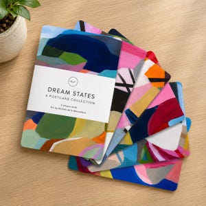 Pode incluir: Um conjunto de seis postais intitulado Dream States: A Postcard Collection, com designs abstratos pintados em cores vibrantes, incluindo azul, rosa, verde e laranja. O cartão superior tem uma faixa branca com texto preto descritivo.