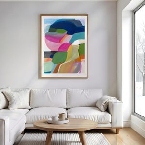 a modern living room with a large abstract painting hanging on the wall above a white sofa. The painting has a vibrant mix of colors and shapes, creating a lively and dynamic atmosphere in the room.