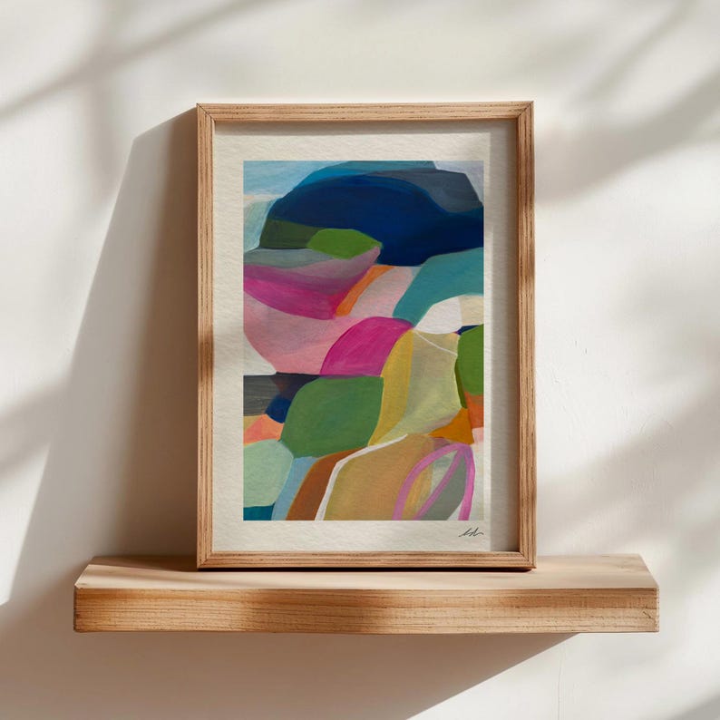 a vibrant abstract painting with a variety of colors and shapes, displayed on a wooden shelf against a white wall.