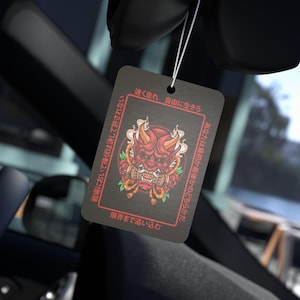 May include: Black rectangular air freshener featuring a red Oni mask design with horns and flames. Japanese text is printed on the air freshener. The air freshener hangs from a white string.