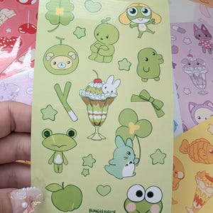 May include: A sheet of stickers with various green cartoon characters and objects, including a frog, a bear, a bunny, and a parfait. The stickers are on a light green background, with the text "BUNGEENOOS" at the bottom.