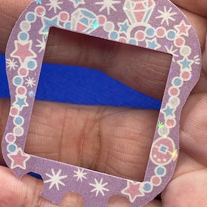 Könnte beinhalten: Ein lila- und rosafarbener, gemusterter Plastikrahmen mit einem klaren Zentrum. Der Rahmen ist mit Sternen, Diamanten und einer Perlenkette verziert.