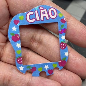 以下が含まれることがあります： 四角い窓と白い文字で「CIAO」と書かれた青と白のステッカー。ステッカーは、チェリー、イチゴ、星、ハートで飾られています。
