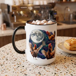 May include: A white ceramic mug with a black handle and rim, filled with a hot beverage topped with marshmallows. The mug features a graphic print of three brown chickens against a dark, starry night sky with a large, glowing full moon.