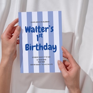 Może przedstawiać: Niebiesko-biała karta zaproszenia na pierwsze urodziny Waltera. Tekst na karcie brzmi "PLEASE JOIN US TO CELEBRATE" i zawiera datę, godzinę, adres i informacje RSVP. Karta jest trzymana przez dwie ręce.