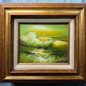 May include: An oil painting of a turbulent ocean scene with crashing waves in shades of green and yellow, featuring two birds in the sky. The artwork is encased in a thick, multi-layered wooden frame with gold-toned inner trim and a beige border.