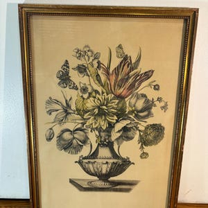 May include: A framed botanical print featuring a detailed illustration of a floral arrangement in a decorative vase. The artwork showcases a variety of flowers and butterflies, rendered in shades of black, white, green, and muted colors, set against a beige background.