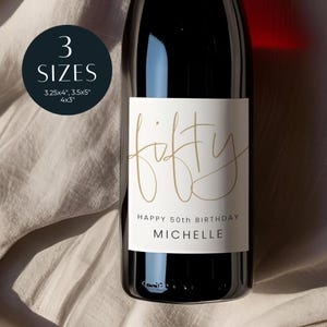 Könnte beinhalten: Eine dunkle Weinflasche mit einem weißen Etikett. Das Etikett trägt das Wort "fifty" in goldener Schrift, darunter "Happy 50th Birthday" und der Name "Michelle". Ein dunkelblauer Kreis zeigt "3 GRÖSSEN" und Abmessungen.