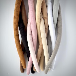 May include: A collection of eight plush fabric tails in various colors, including brown, black, pink, beige, and gray. The tails are all about 12 inches long and are made of soft, fluffy fabric.