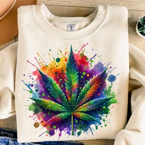 May include: Cream-coloured sweatshirt with a colourful cannabis leaf design. The leaf is in green, yellow, orange, and red, with a watercolour splash effect. A unique and eye-catching graphic, perfect for casual wear.