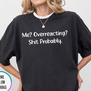 May include: A black short-sleeved t-shirt featuring the white text Me? Overreacting? Shit Probably. The shirt has a crew neckline and a loose fit. A small circular graphic with the text More Color Options is visible on the left side.