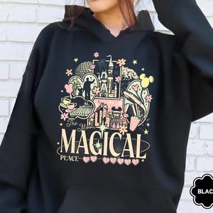 May include: Black hooded sweatshirt with a colorful graphic featuring a castle, Mickey Mouse ears, and the text "The Most Magical Place." The design includes pink, yellow, and black elements. The sweatshirt has a front pocket.