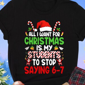 May include: Black t-shirt with the text "ALL I WANT FOR CHRISTMAS IS MY STUDENTS TO STOP SAYING 6-7" in green and red. The shirt features a Santa hat and candy cane design. Plaid pajama pants and a wrapped gift are also visible.
