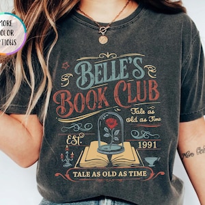 Pu&ograve; includere: T-shirt grigio scuro con un design vintage. La maglietta presenta il testo "Belle's Book Club" in blu e rosso, insieme alla frase "Tale as old as Time" e all'anno "1991". &Egrave; raffigurata anche una rosa in una cupola di vetro.