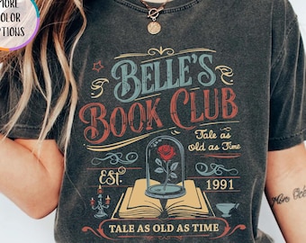 May include: A dark gray t-shirt with a vintage design. The shirt features the text "Belle's Book Club" in blue and red, along with the phrase "Tale as old as Time" and the year "1991". A rose in a glass dome is also depicted.