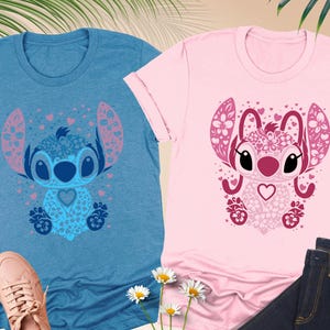 May include: Two short-sleeved t-shirts, one blue and one pink, each featuring a cartoon character design. The blue shirt has a blue and pink character design, while the pink shirt has a pink and maroon character design. The shirts are paired with jeans and sneakers.