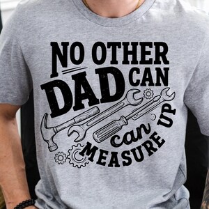 May include: Gray athletic heather t-shirt with the text "NO OTHER DAD CAN MEASURE UP" in black. The design includes illustrations of a hammer, wrench, screwdriver, and gears.