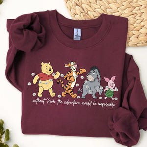Puede incluir: Sudadera granate con una ilustraci&oacute;n de Winnie the Pooh y sus amigos. El dise&ntilde;o incluye a Pooh, Tigger, Eeyore y Piglet, con el texto "without Pooh the adventure would be impossible". Cuello redondo y mangas largas.