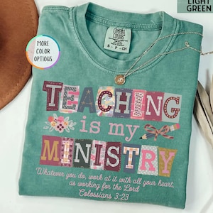 May include: Light green t-shirt with the words "TEACHING is my MINISTRY" in colorful block letters. The shirt also features a floral design and the Bible verse Colossians 3:23. A gold necklace is draped across the shirt.