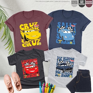 May include: Four children's t-shirts with Cars movie characters. The shirts are in shades of maroon, navy, dark grey, and athletic heather. Each shirt features a different car character with text and checkered flags, evoking a racing theme.